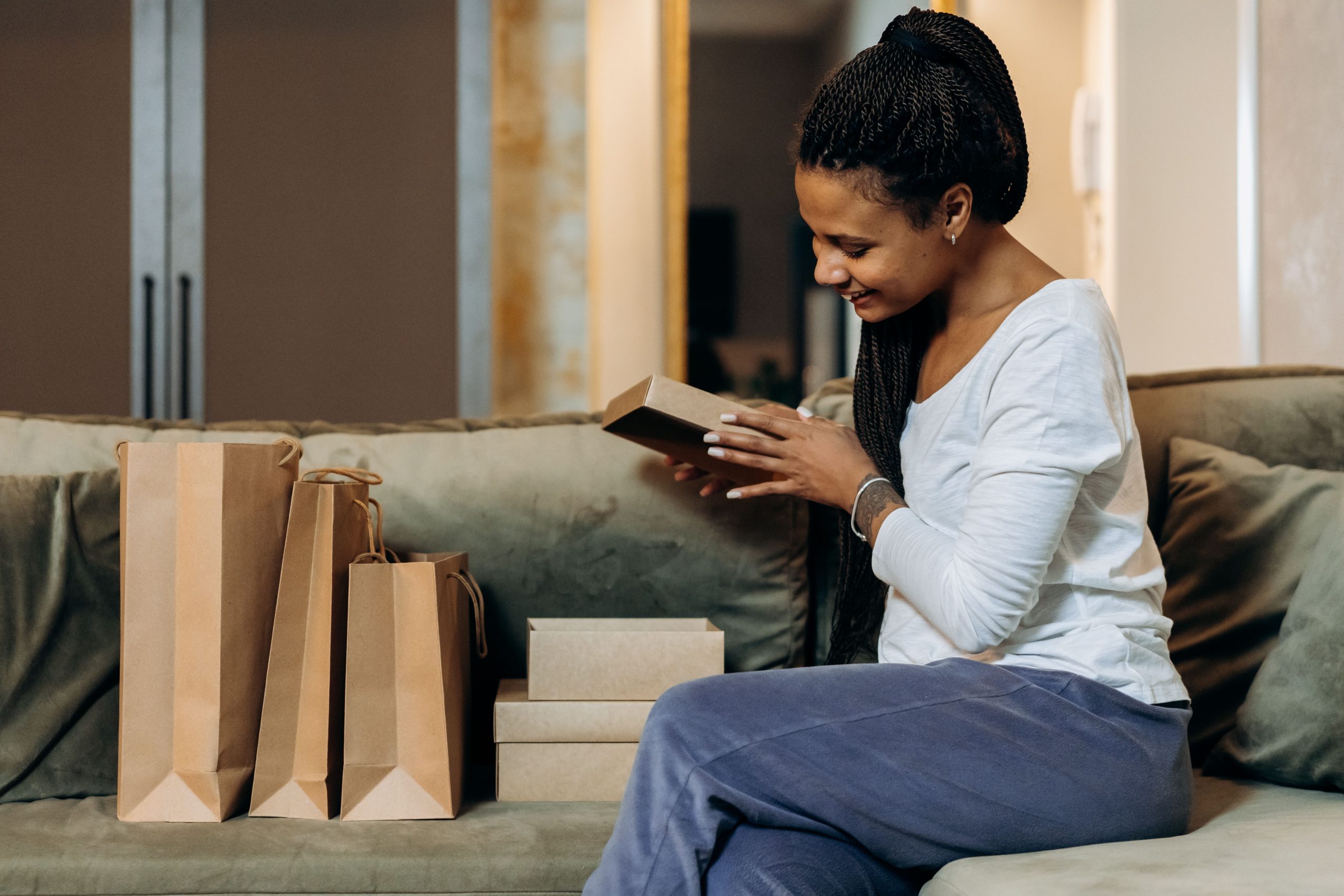 Femme souriante deballe des cadeaux sur canapé