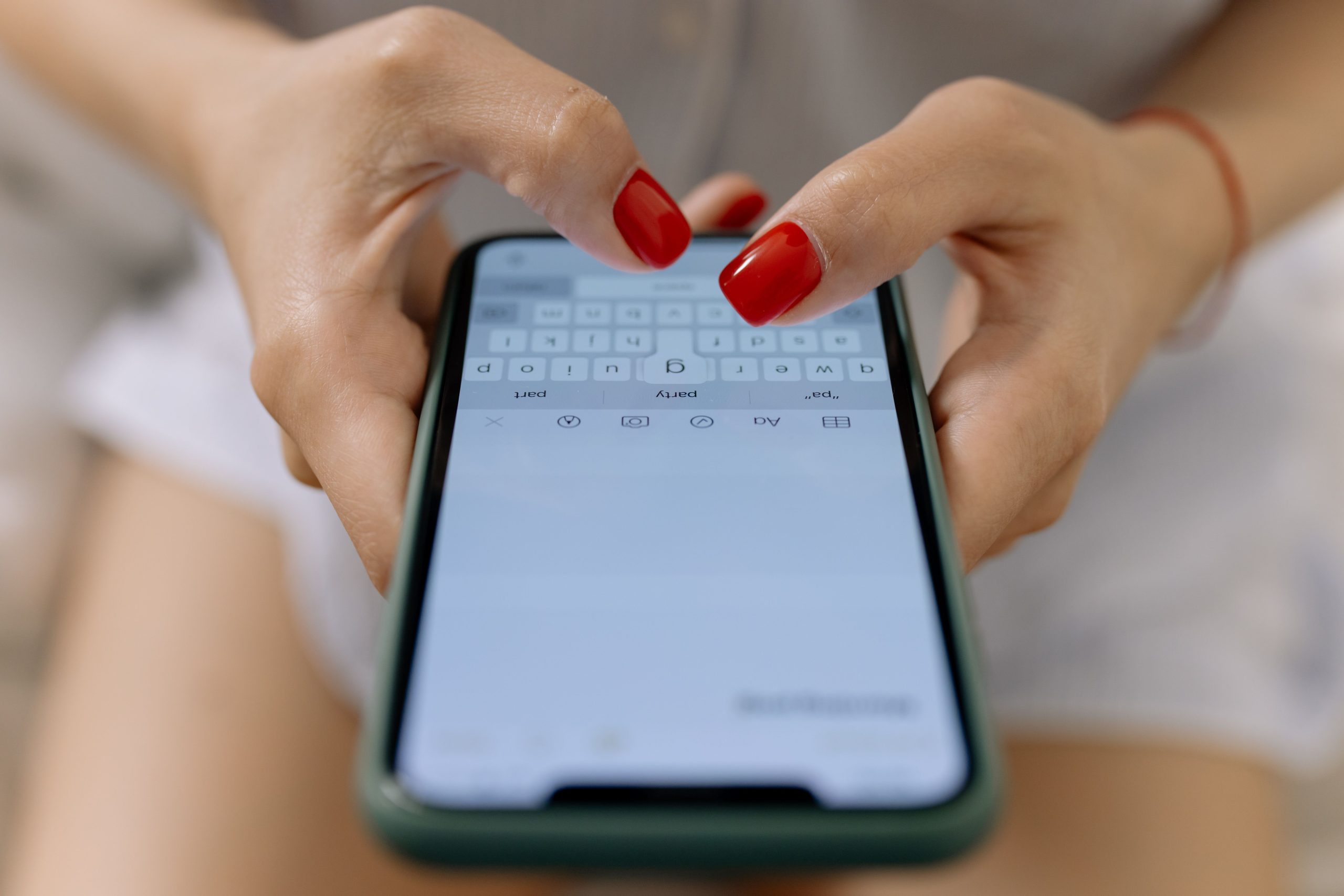 Mains aux ongles rouges tapant sur écran smartphone